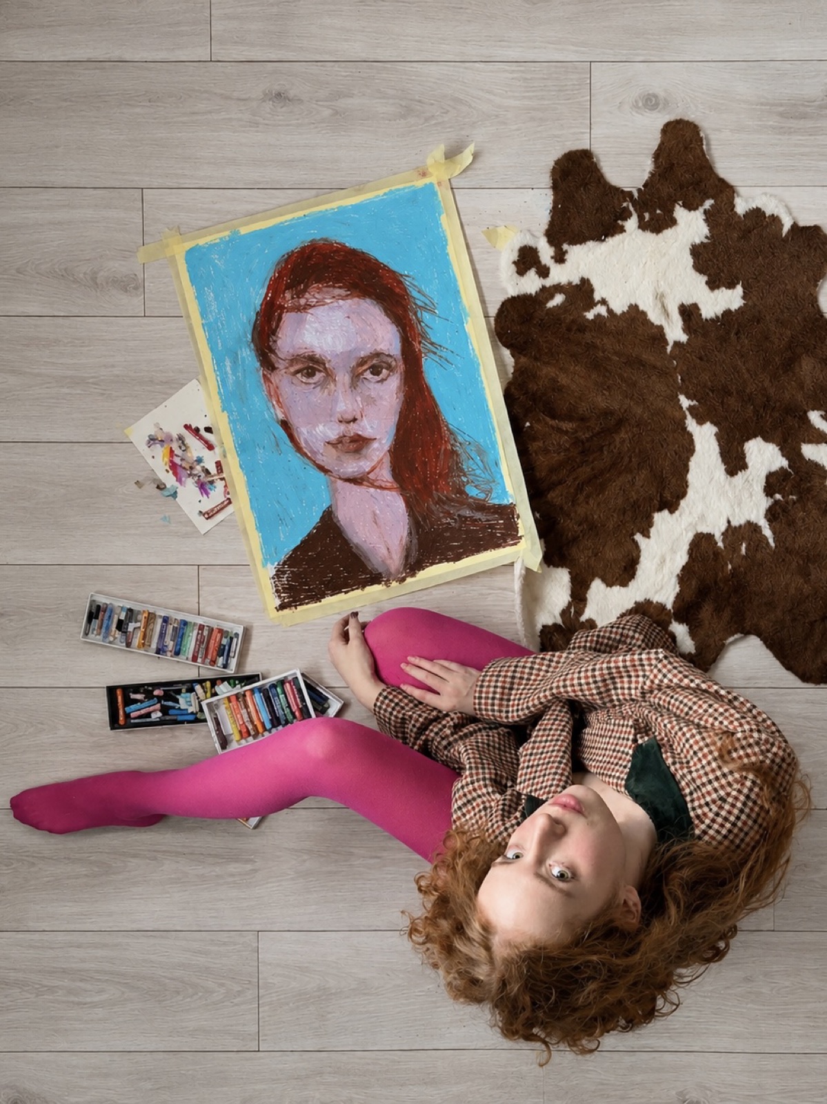 Anastasija Aleksejeva on the floor next to her oil pastel portrait