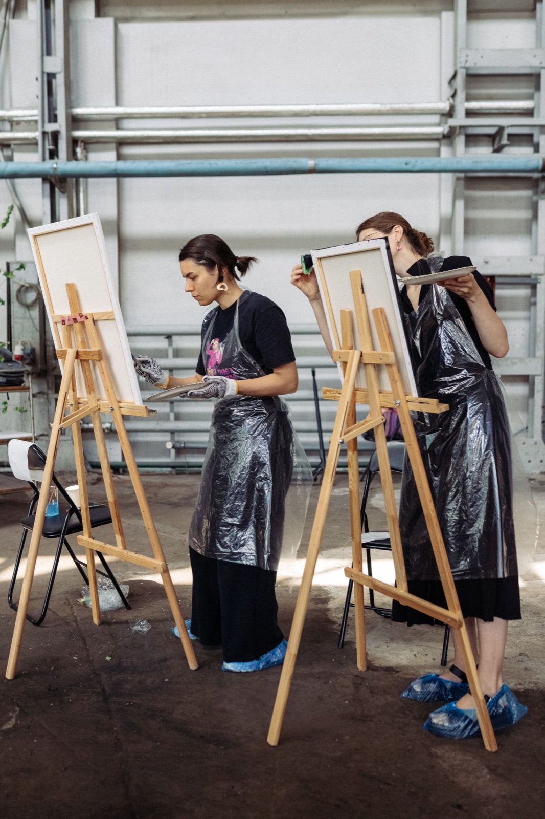 Two participants painting at easels in an industrial space